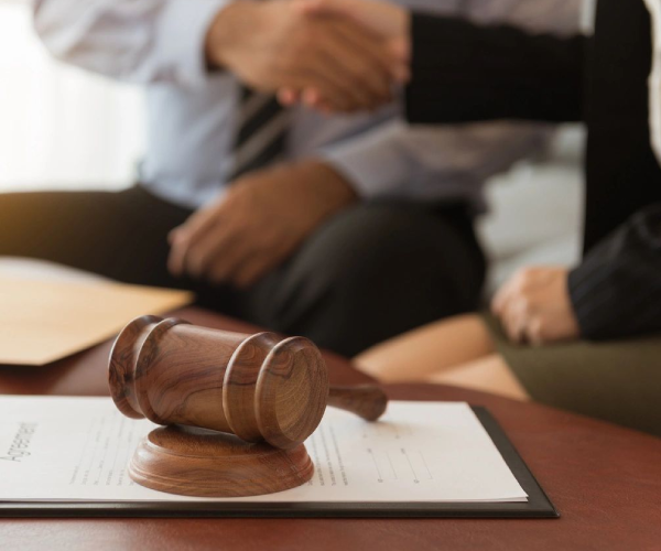 Gavel on contract with handshake behind